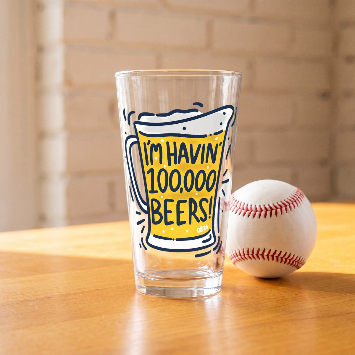 100,000 Beers Pint Glass on a wood table next to a baseball